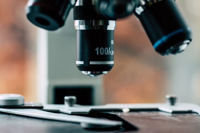 A medical researcher examines a vial of Talquetamab drug in a laboratory setting with microscopes and equipment nearby.