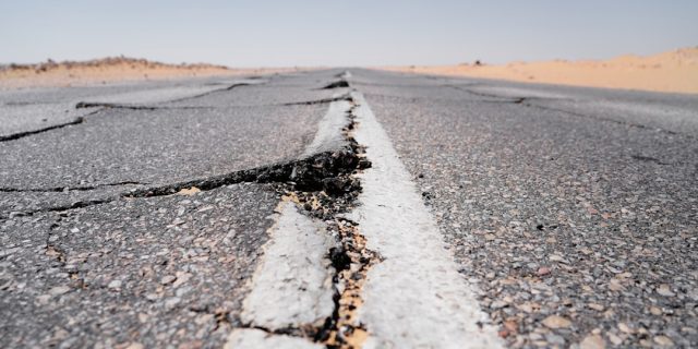Cracked asphalt on a quiet Ojai street after the 2023 quake, with residents inspecting minor damage under sunny skies.