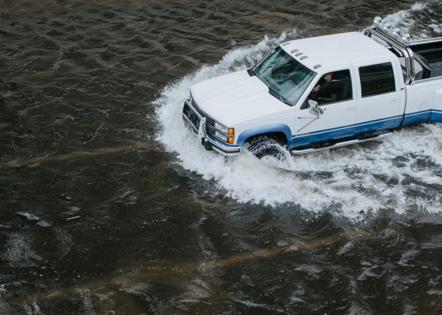 A flooded street in southern Florida with water rising near homes and vehicles under a dark storm sky.