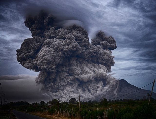 Ash plume rising from Hayli Gubbi volcano in Ethiopia's Afar Region, with grounded airplanes visible on a distant tarmac.