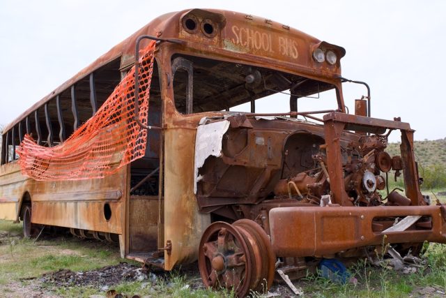 A crumpled bus and trailer wreckage on a dusty road in Khairpur, with emergency workers assessing the scene.