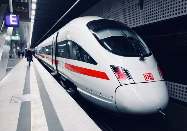 A high-speed train speeds past green Indonesian countryside, with passengers boarding at a modern station.