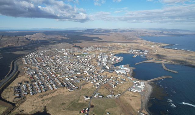 Aerial view of a volcanic fissure emitting lava near the town of Grindavík, Iceland, with smoke rising over residential areas.