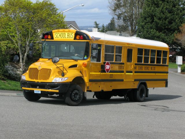 Overturned yellow school bus on a road in The Wirral, England, with emergency responders and debris visible around the crash site.