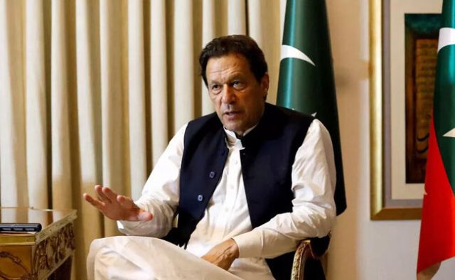 Imran Khan addressing a crowd at a political rally in Pakistan, gesturing with his hand while supporters wave flags.