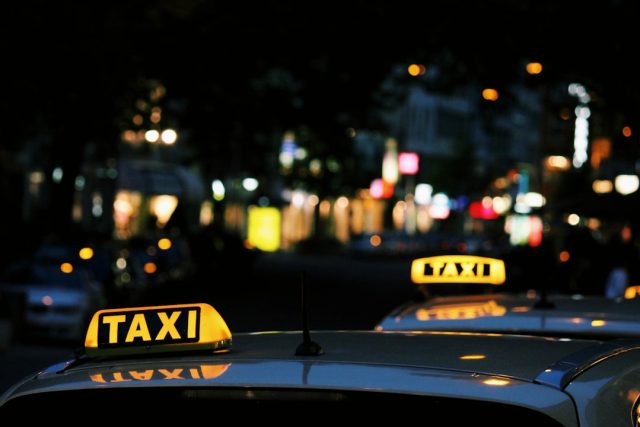 Ola ride-hailing app interface on a smartphone with London black cabs in the background