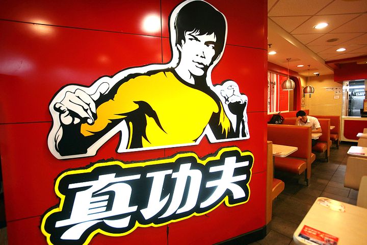 Real Kungfu Bruce Lee Logo Shannon Lee stands at a podium holding a photo of her father Bruce Lee beside the Real Kungfu restaurant logo for comparison.