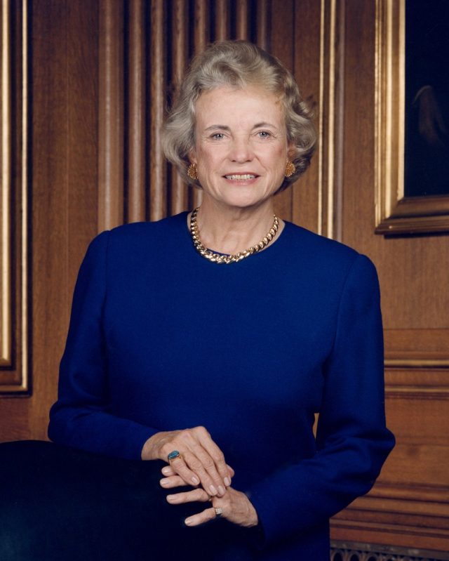 Sandra Day O'Connor in her judicial robe, standing before the U.S. Supreme Court building with a determined expression.