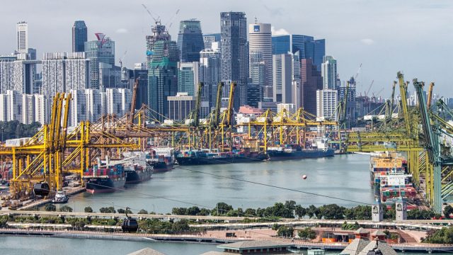 Container ship docked at Singapore port with cranes loading cargo under a cloudy sky.