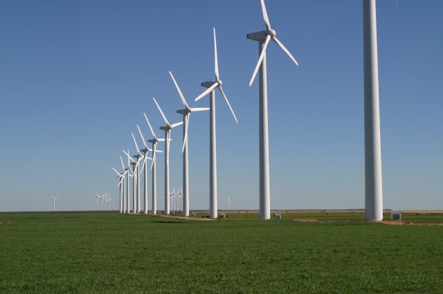 Wind turbines spinning on a green hillside under a blue sky, representing renewable energy growth in the United States.