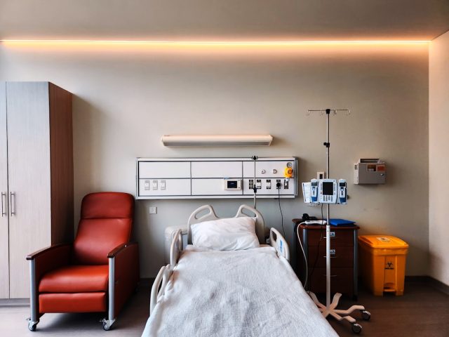 A cancer patient in a hospital bed holds a plate of food while a doctor reviews a chart showing weight gain data from a ponsegromab trial.