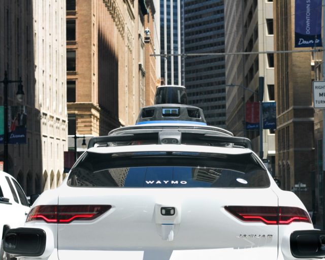 A Waymo autonomous vehicle drives through a city street with no driver behind the wheel during a paid passenger ride.